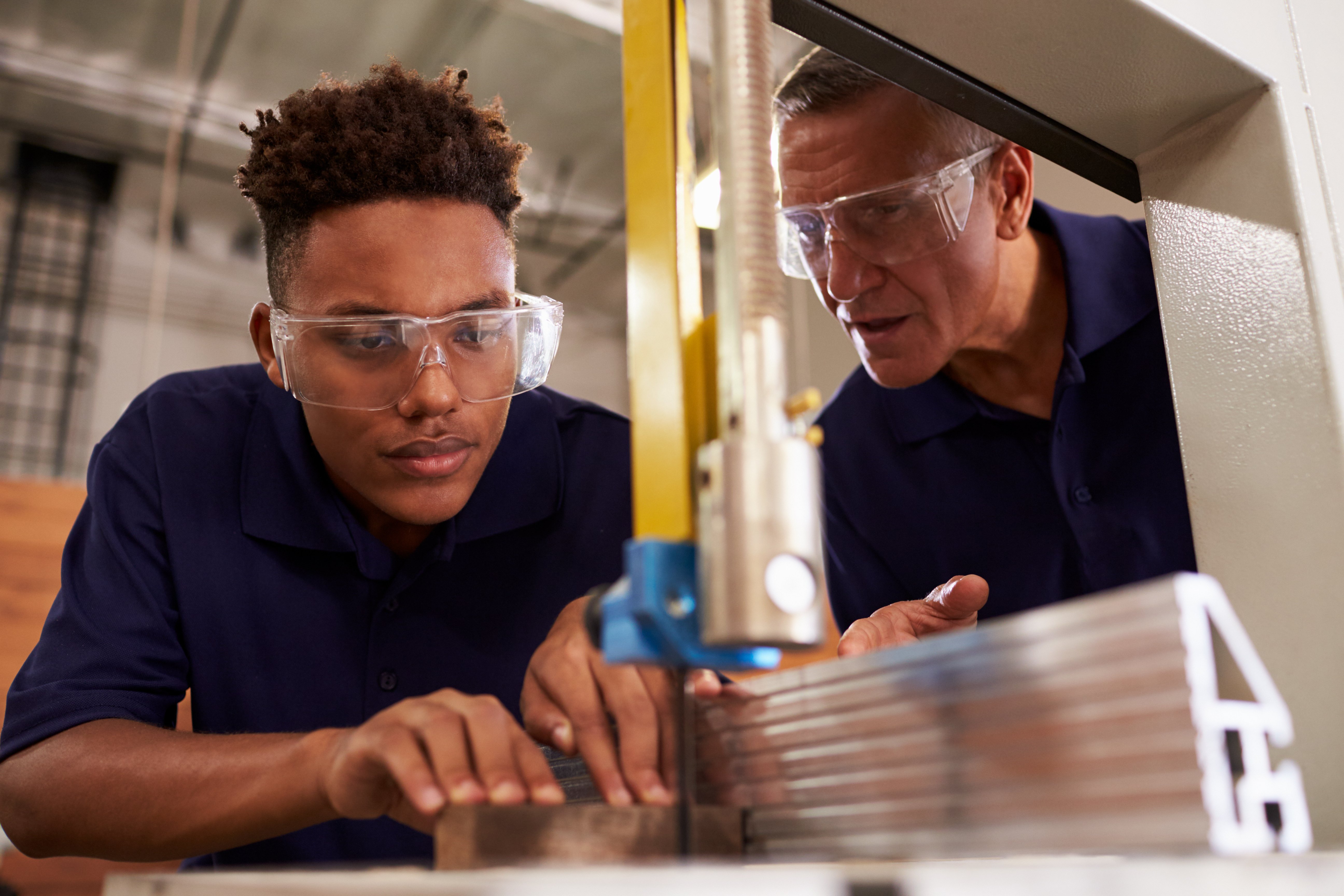 Skilled trades apprentice receiving hands-on training while using a mechanized saw with an experienced carpenter.